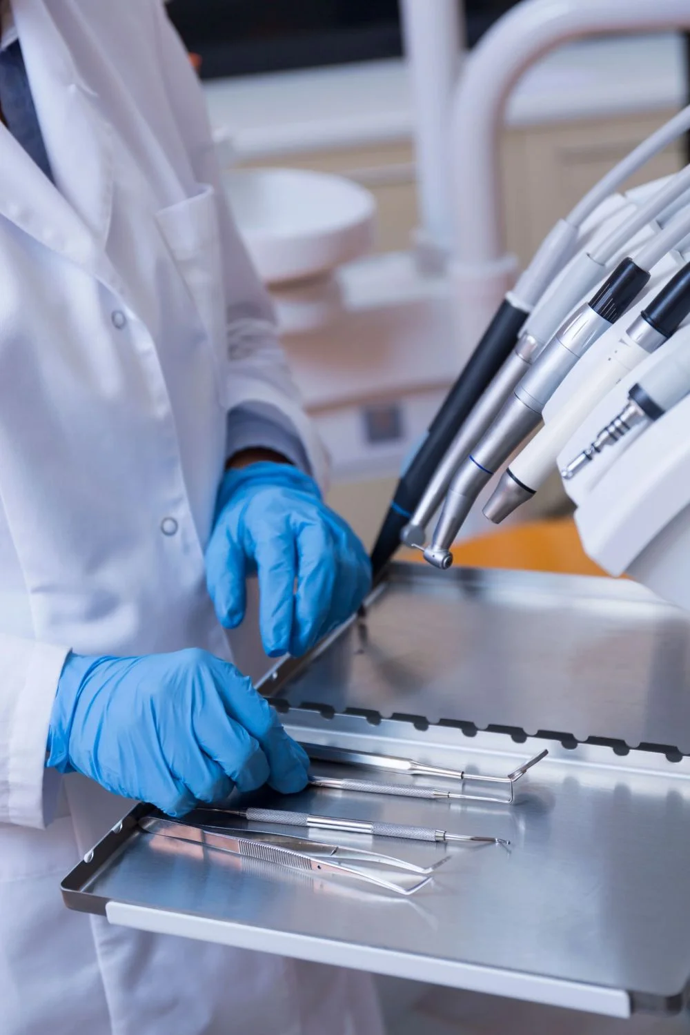 Eine behandschuhte Hand legt ein Tablett mit zahnmedizinischen Instrumenten aus Metall in ein Sterilisationsgerät mit offener Tür, um optimale Hygiene für die Patientenversorgung zu gewährleisten.